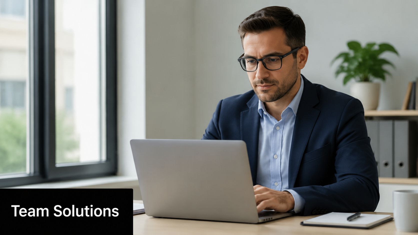 A professional man in a business suit working on his laptop in a bright office environment.